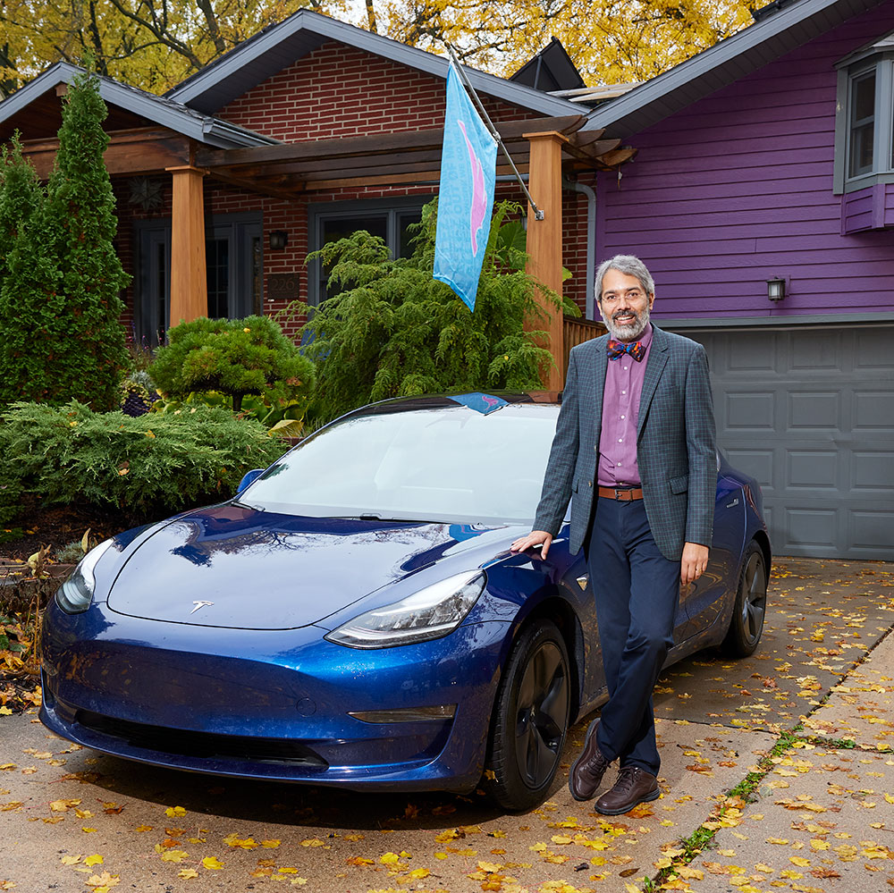 Dipesh Navsaria, a participant in MGE's Charge Ahead program, stands beside his blue Tesla outside of his home.