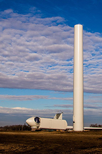 A rotor and nacelle rest next to one of Saratoga's towers.