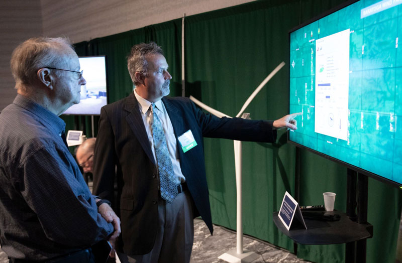 A shareholder talks with MGE's Dan Clausen by a display featuring energy production data from MGE's Saratoga Wind Farm.